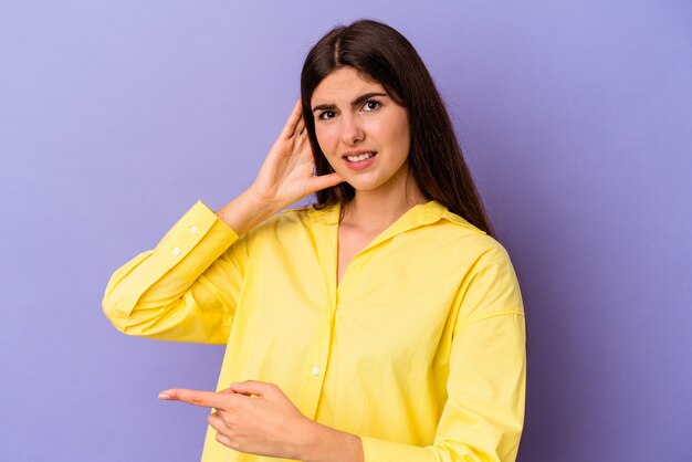 Young caucasian woman isolated on purple background trying to listening a gossip.