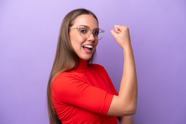 Young caucasian woman isolated on purple background With glasses and celebrating a victory