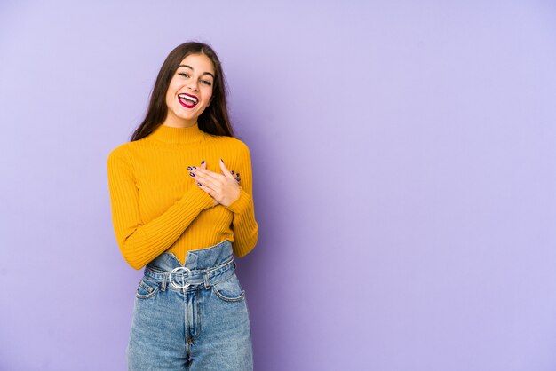 Young caucasian woman isolated on purple has friendly expression, pressing palm to chest. Love concept.