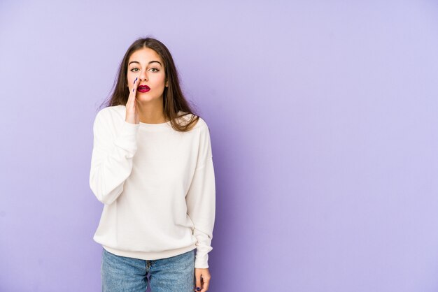 Young caucasian woman isolated on purple is saying a secret hot braking news and looking aside