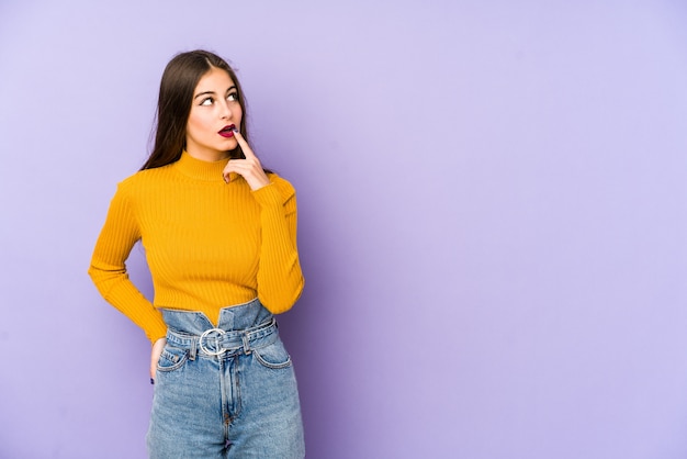 Young caucasian woman isolated on purple looking sideways with doubtful and skeptical expression.