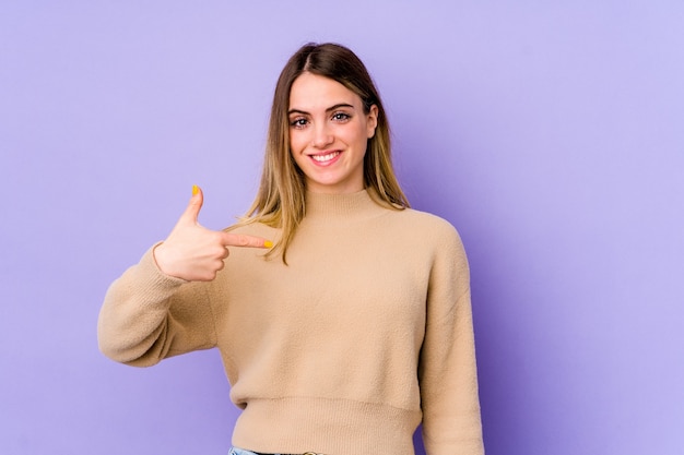 Young caucasian woman isolated on purple person pointing by hand to a shirt copy space, proud and confident