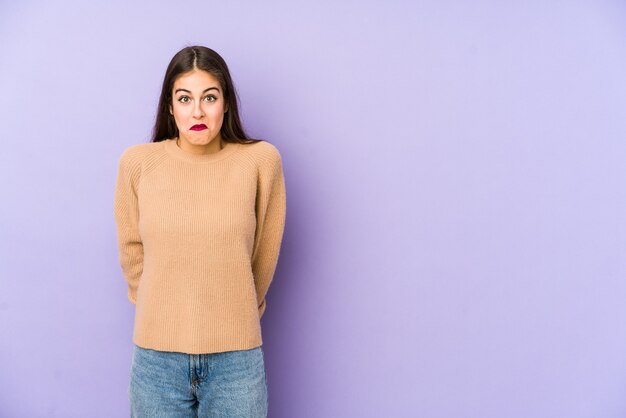 Young caucasian woman isolated on purple space shrugs shoulders and open eyes confused.