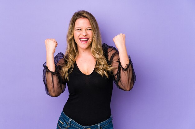 Young caucasian woman isolated on purple wall cheering carefree and excited. Victory concept.