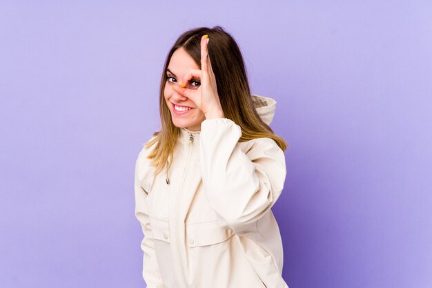 Young caucasian woman isolated on purple wall excited keeping ok gesture on eye.