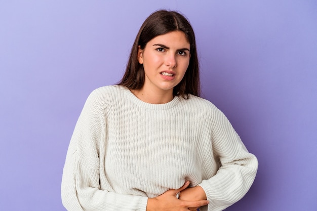 young caucasian woman isolated on purple wall having a liver pain, stomach ache.