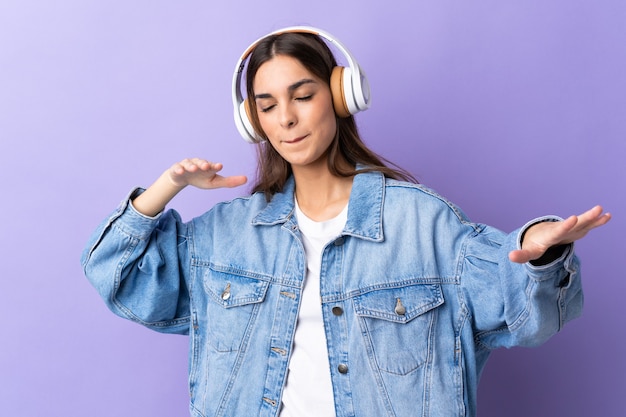 Giovane donna caucasica isolata sulla parete viola ascoltando musica e balli