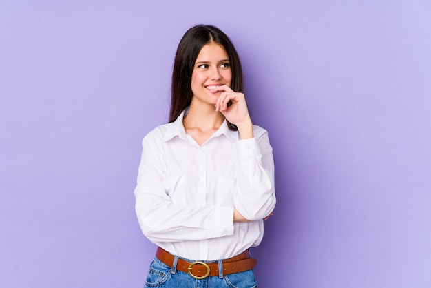 Young caucasian woman isolated on purple wall relaxed thinking about something looking at a copy space