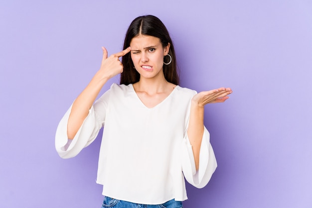 Young caucasian woman isolated on purple wall showing a disappointment gesture with forefinger.