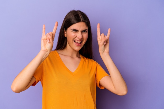 Young caucasian woman isolated on purple wall showing a horns gesture