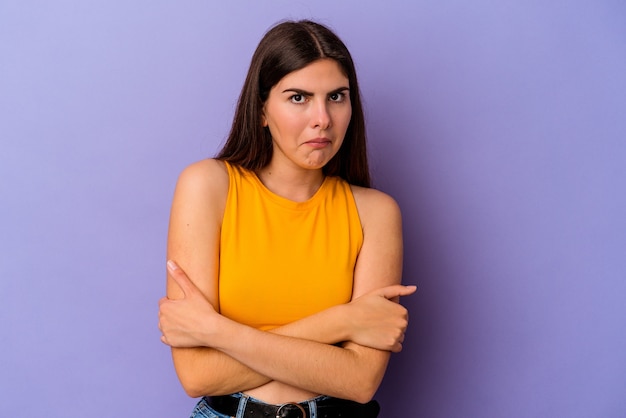 Young caucasian woman isolated on purple wall shrugs shoulders and open eyes confused.