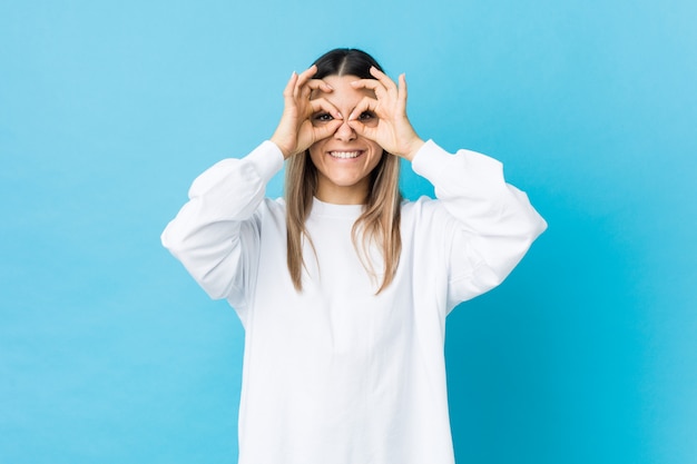 Young caucasian woman isolated showing okay sign over eyes