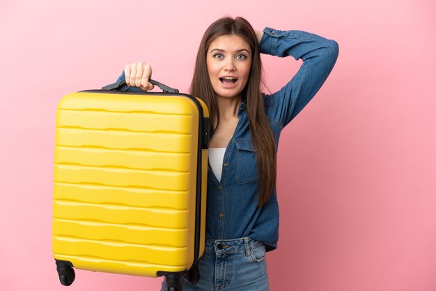 Young caucasian woman isolated in vacation with travel suitcase and surprised