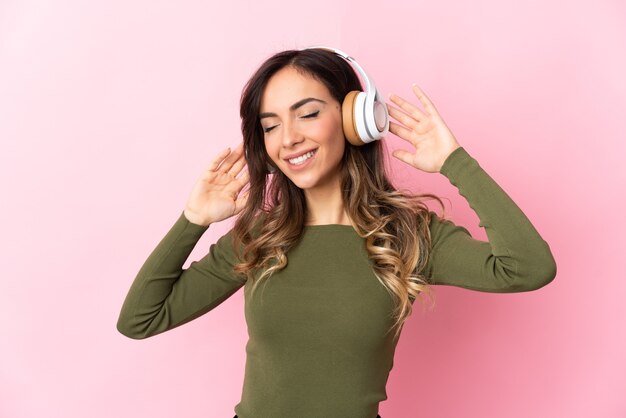 Young caucasian woman over isolated wall listening music with a mobile and singing