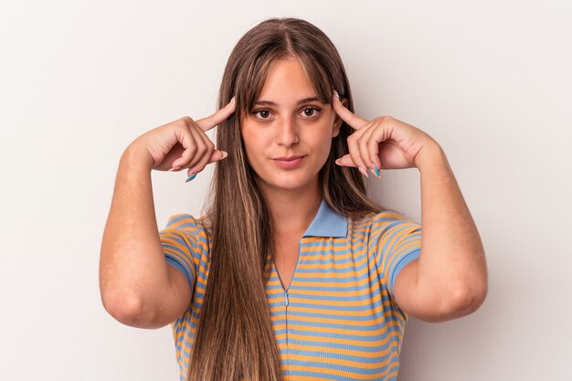 白い背景で隔離された若い白人女性は、人差し指を頭に向けたまま、タスクに焦点を当てました。