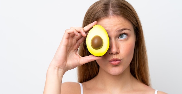 Young caucasian woman isolated on white background holding an avocado Close up portrait