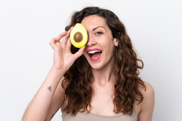 Young caucasian woman isolated on white background holding an avocado while smiling Close up portrait