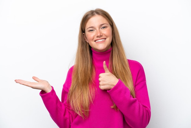 Young caucasian woman isolated on white background holding copyspace imaginary on the palm to insert an ad and with thumbs up