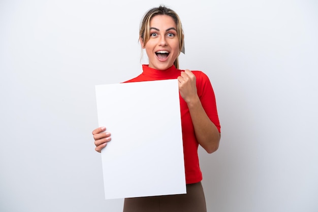 Young caucasian woman isolated on white background holding an empty placard and celebrating a victory