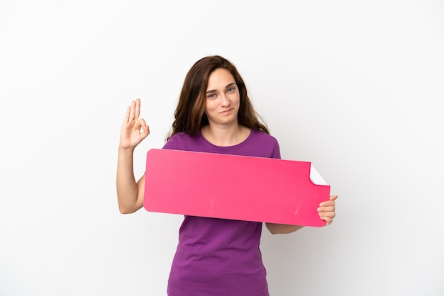 Young caucasian woman isolated on white background holding an empty placard and doing OK sign