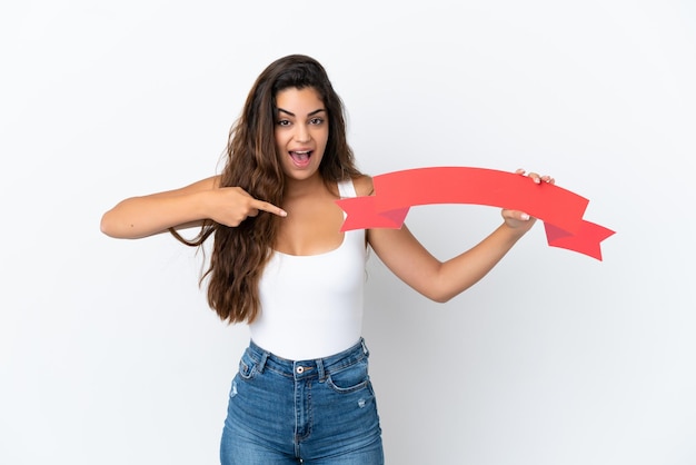 Young caucasian woman isolated on white background holding an empty placard with surprised expression