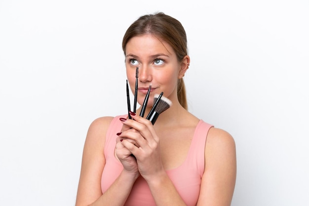 Photo young caucasian woman isolated on white background holding makeup brush and looking up