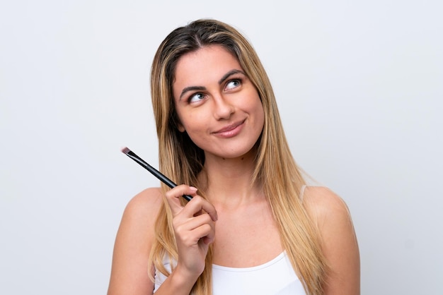 Young caucasian woman isolated on white background holding makeup brush and looking up