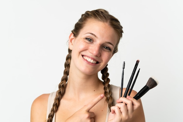 Young caucasian woman isolated on white background holding makeup brush and pointing it