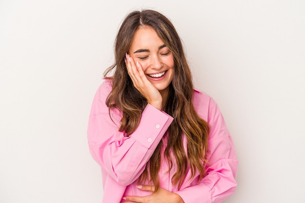 Young caucasian woman isolated on white background laughs happily and has fun keeping hands on stomach.