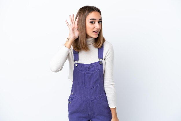 Young caucasian woman isolated on white background listening to something by putting hand on the ear