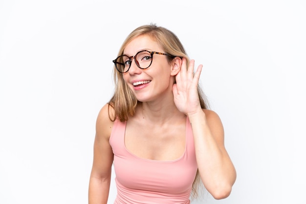 Young caucasian woman isolated on white background listening to something by putting hand on the ear