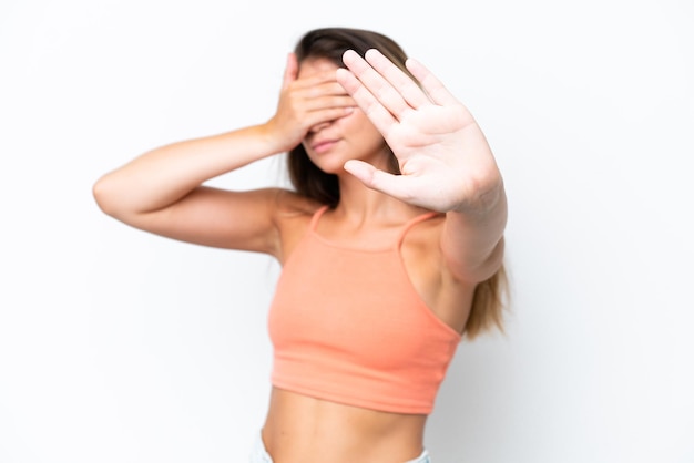 Foto giovane donna caucasica isolata su sfondo bianco che fa il gesto di fermarsi e copre la faccia