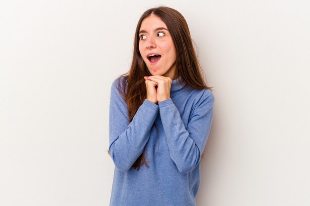 Young caucasian woman isolated on white background praying for luck, amazed and opening mouth looking to front.