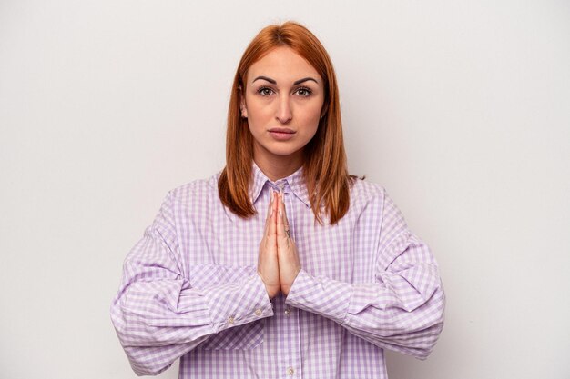 Young caucasian woman isolated on white background praying, showing devotion, religious person looking for divine inspiration.