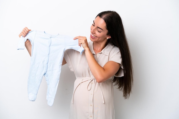 妊娠し、赤ちゃんの服を保持している白い背景で隔離の若い白人女性