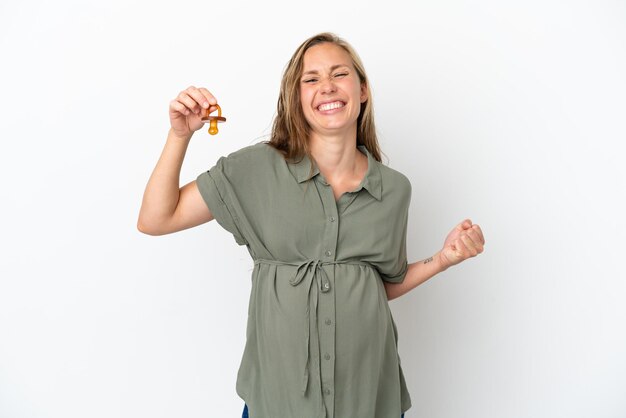 Young caucasian woman isolated on white background pregnant and holding a pacifier and celebrating a victory
