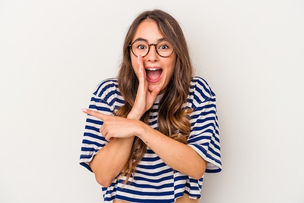 Young caucasian woman isolated on white background saying a gossip, pointing to side reporting something.