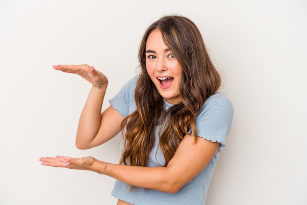 Young caucasian woman isolated on white background shocked and amazed holding a copy space between hands.