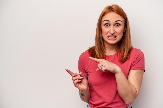 Young caucasian woman isolated on white background shocked pointing with index fingers to a copy space.