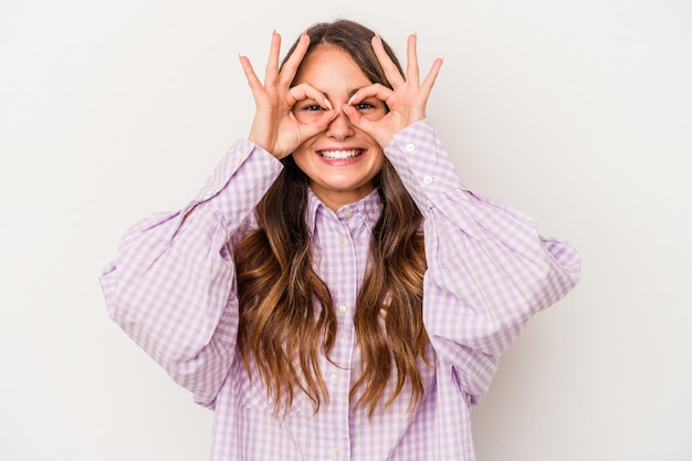 Young caucasian woman isolated on white background showing okay sign over eyes