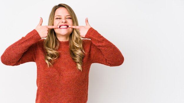 Young caucasian woman isolated on white background smiles, pointing fingers at mouth.