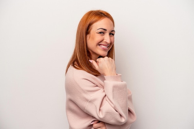Молодая кавказская женщина, изолированная на белом фоне, счастливо и уверенно улыбается, касаясь подбородка рукой