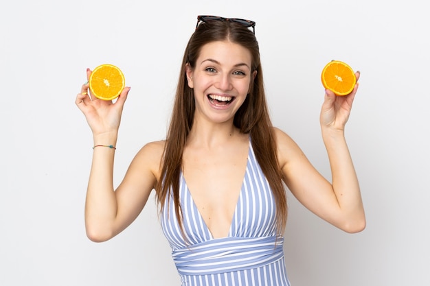 Young caucasian woman isolated on white background in swimsuit and holding an orange