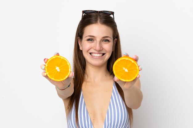 Young caucasian woman isolated on white background in swimsuit and holding an orange