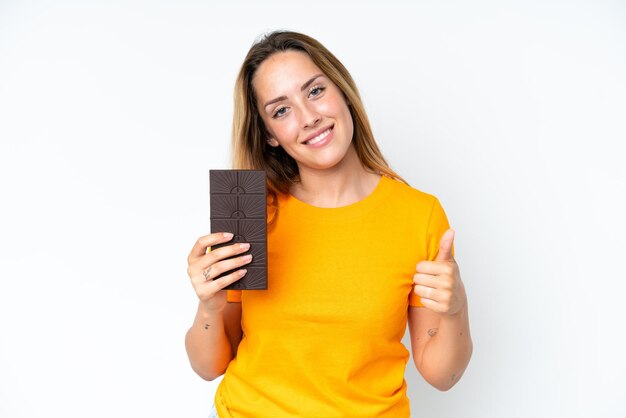 Young caucasian woman isolated on white background taking a chocolate tablet and with thumb up