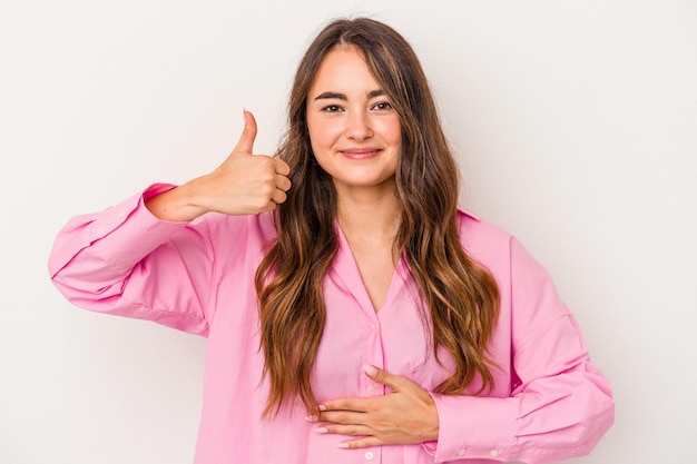 Young caucasian woman isolated on white background touches tummy, smiles gently, eating and satisfaction concept.