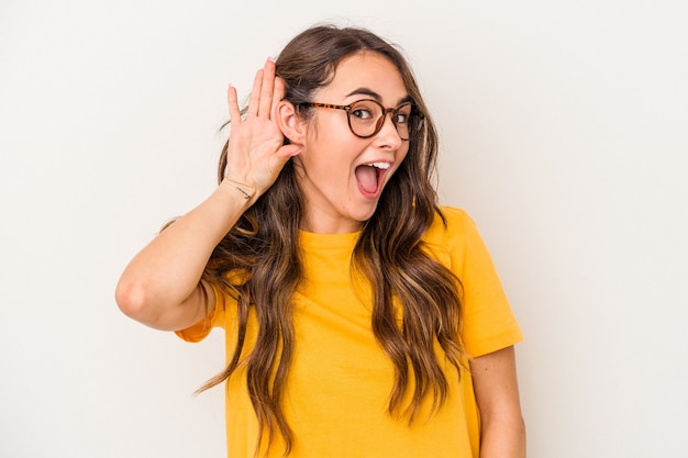 Young caucasian woman isolated on white background trying to listening a gossip.