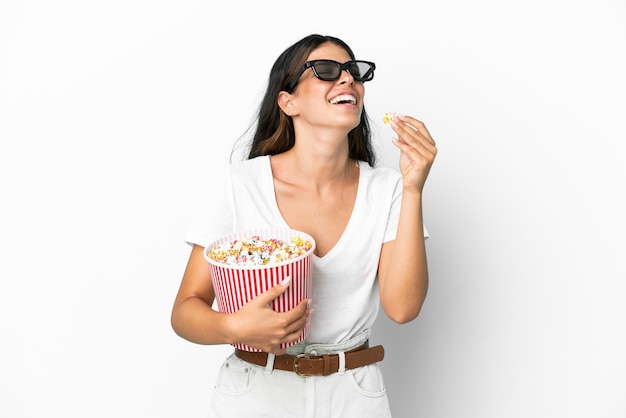 Молодая кавказская женщина изолирована на белом фоне с 3d-очками и держит большое ведро попкорна