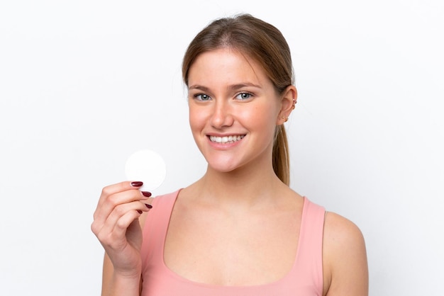 Young caucasian woman isolated on white background with cotton pad for removing makeup from her face and smiling