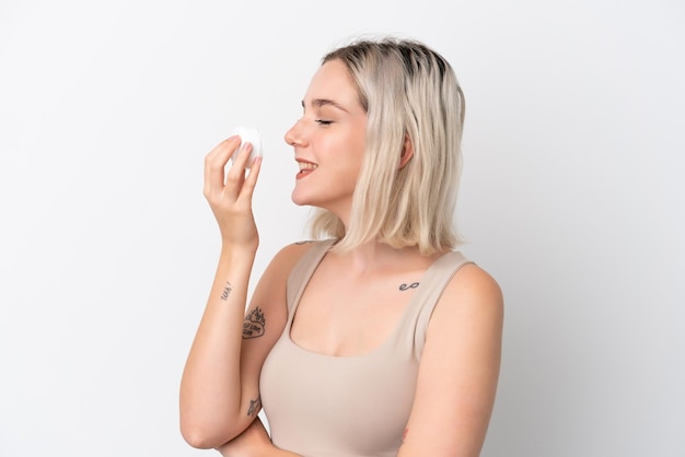 Young caucasian woman isolated on white background with moisturizer and smelling it